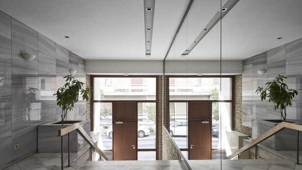 Eine moderne Lobby mit Marmorboden, einer Treppe und großen Glasüren, die nach draußen führen.