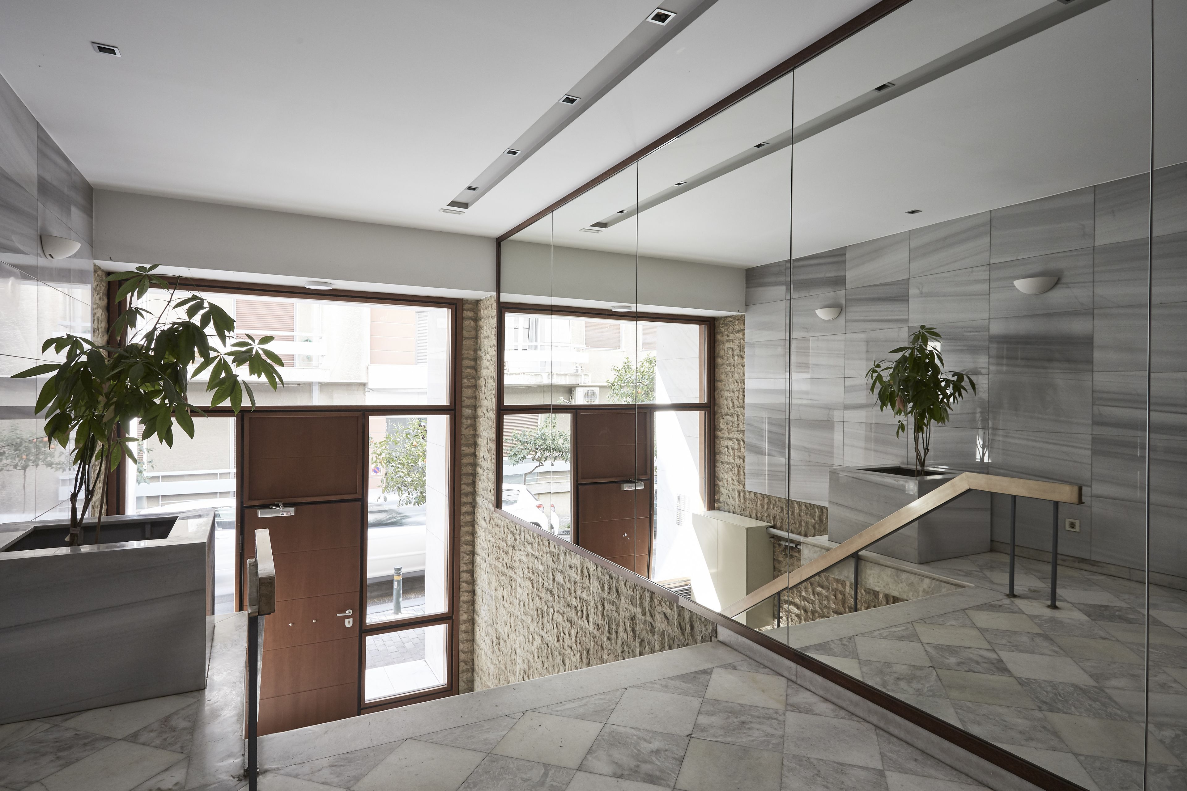 A modern interior with a marble staircase, large windows, and potted plants.
