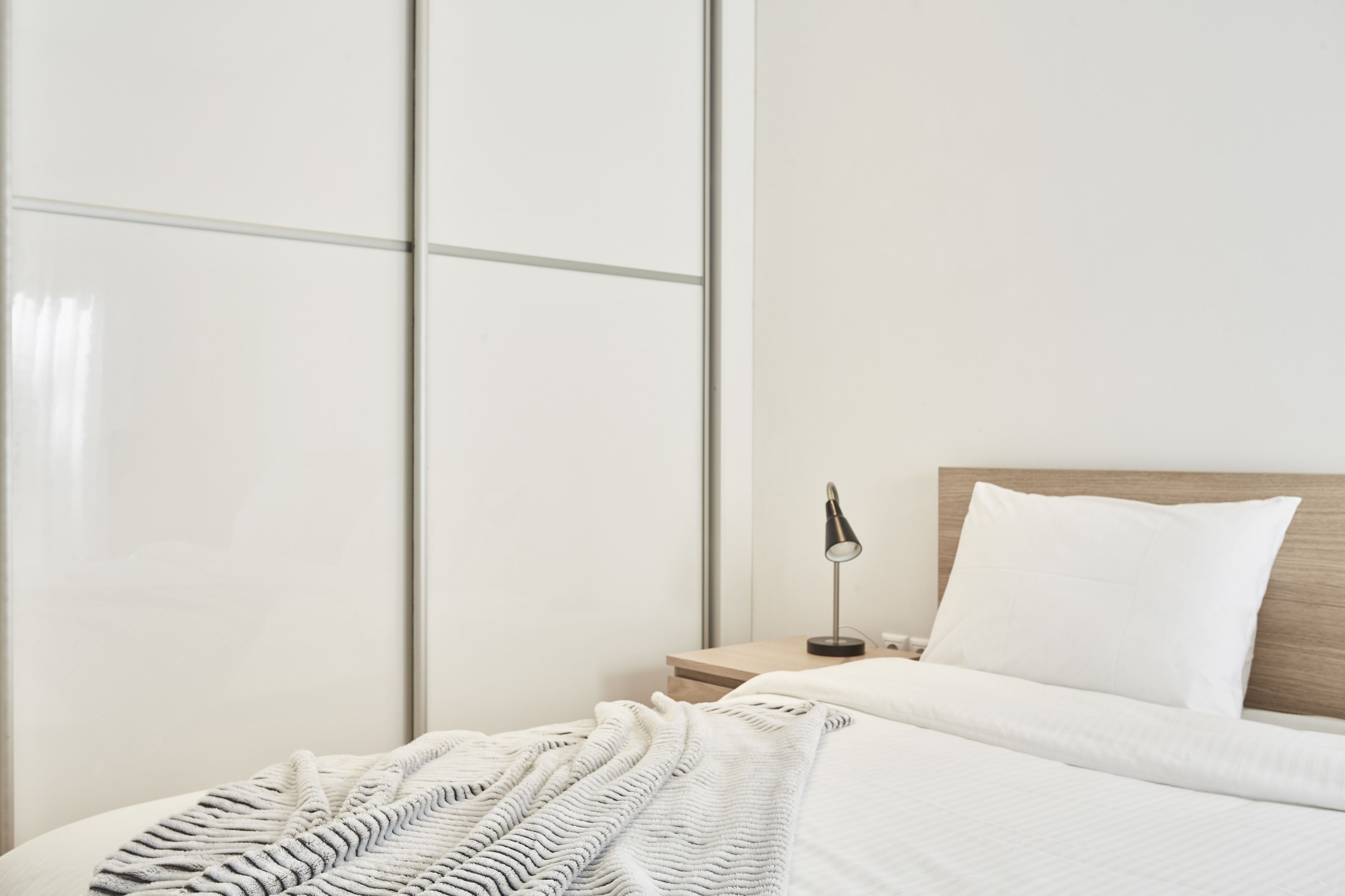 A neatly made bed with white linens, a bedside lamp, and a wooden headboard.