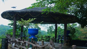 A rustic outdoor seating area with a thatched roof, wooden fence, and a large blue planter. - Senaro Holiday Resort (Udugama)
