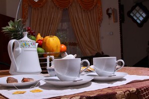A table set with white teacups, saucers, a white teapot, a fruit bowl, and a small plate with pastries. - Senaro Holiday Resort (Udugama)