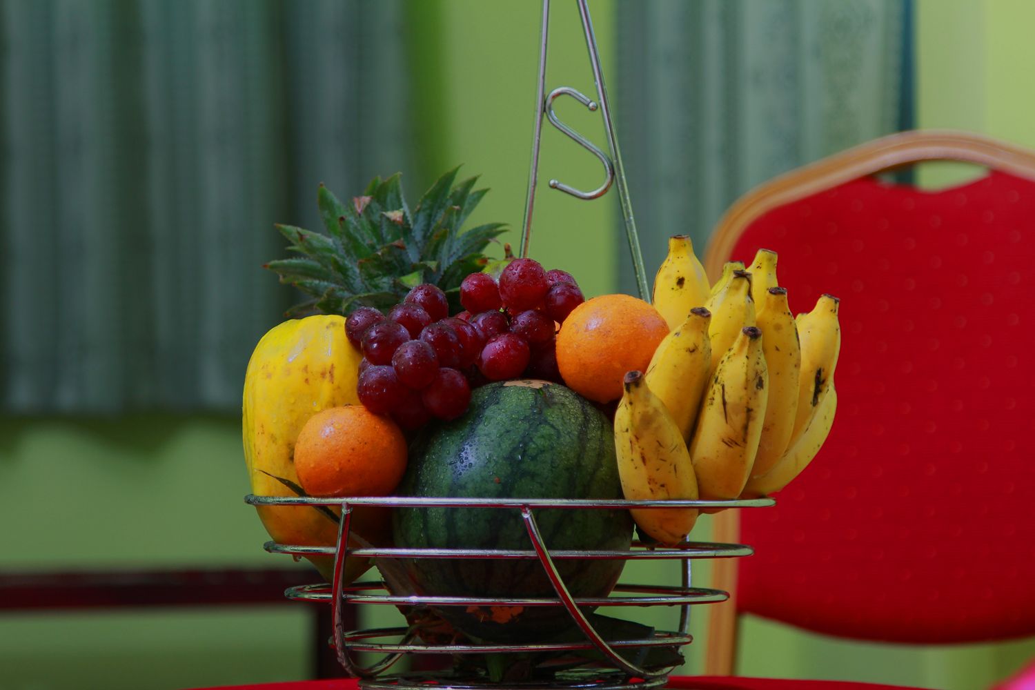 A fruit basket with a pineapple, grapes, oranges, bananas, and a watermelon.