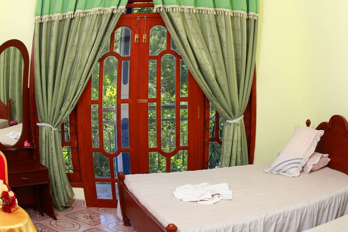A bedroom with a bed, a wooden wardrobe, a mirror, and a window with curtains.