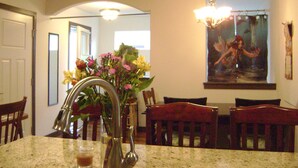 Un comedor con una mesa de mármol, sillas, un jarrón con flores y un cuadro en la pared.