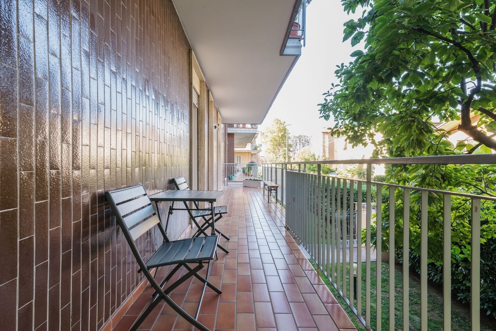 A balcony with a table and chairs, a tiled floor, and a metal railing.