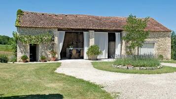 A stone building with a tiled roof, a gravel driveway, and a grassy lawn.