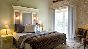 A bedroom with a large bed, two bedside lamps, a stone wall, and a view of the outdoors. - Domaine de L'Isle Basse (Fontanes)