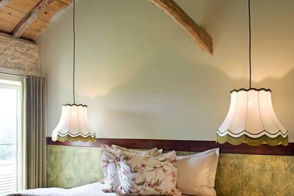 A bedroom with a wooden ceiling, a bed with floral pillows, and two hanging lamps.