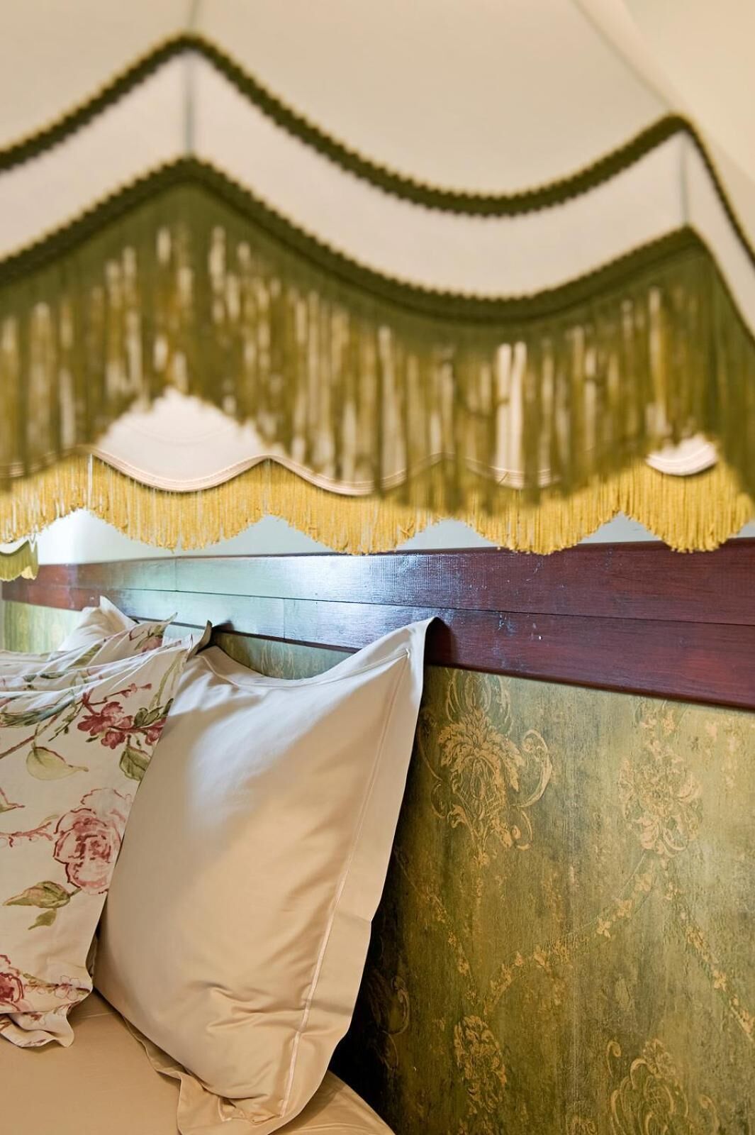 Una cama con un cojín floral y un cabecero verde con detalles decorativos.