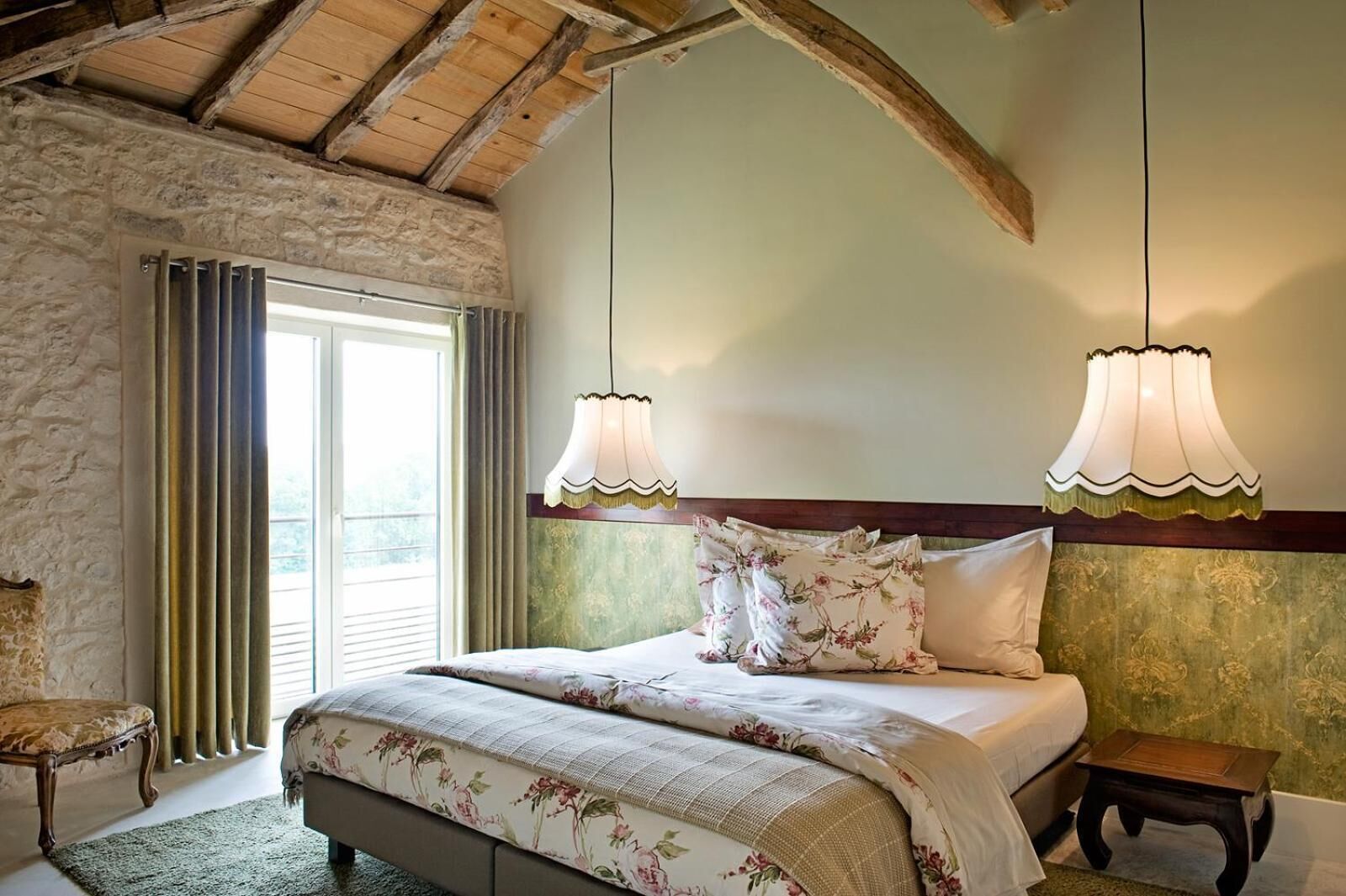 A bedroom with a large bed, two wall-mounted lamps, a wooden headboard, and a stone wall.