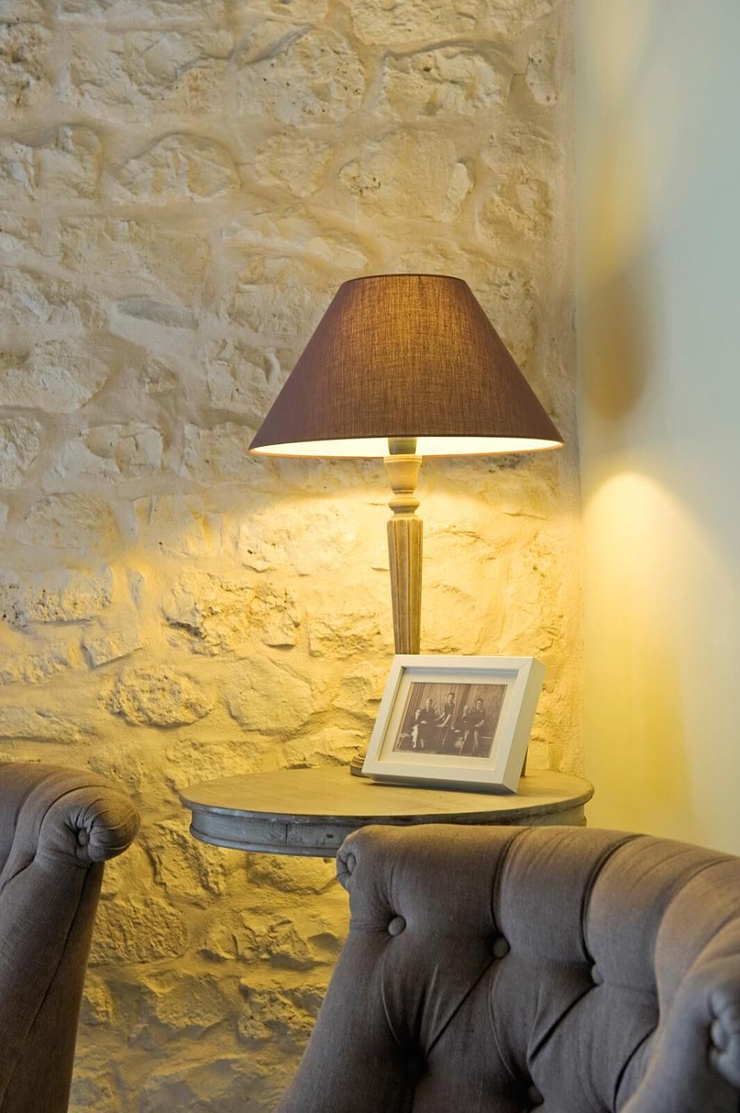 Luminária com cúpula marrom sobre uma mesa pequena, em frente a uma parede de pedra com textura.