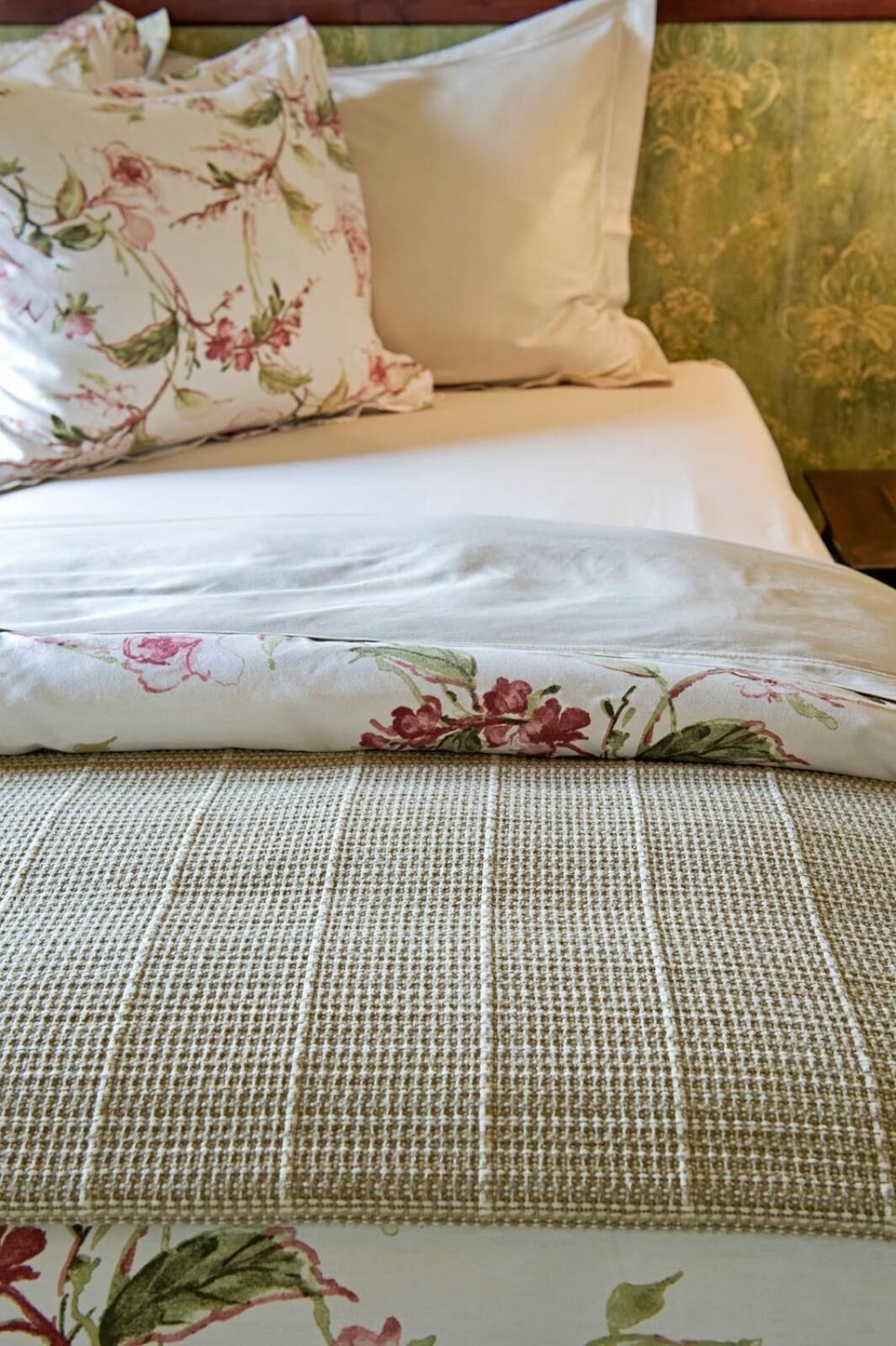Una cama bien hecha con ropa de cama de estampado floral y una manta texturizada.