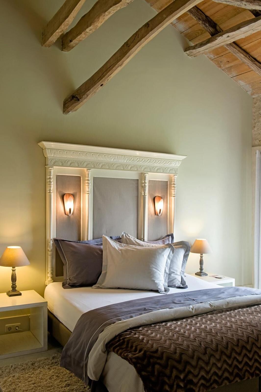 Un dormitorio con una cama grande, dos lámparas de noche, un cabecero decorativo y una viga de techo de madera.