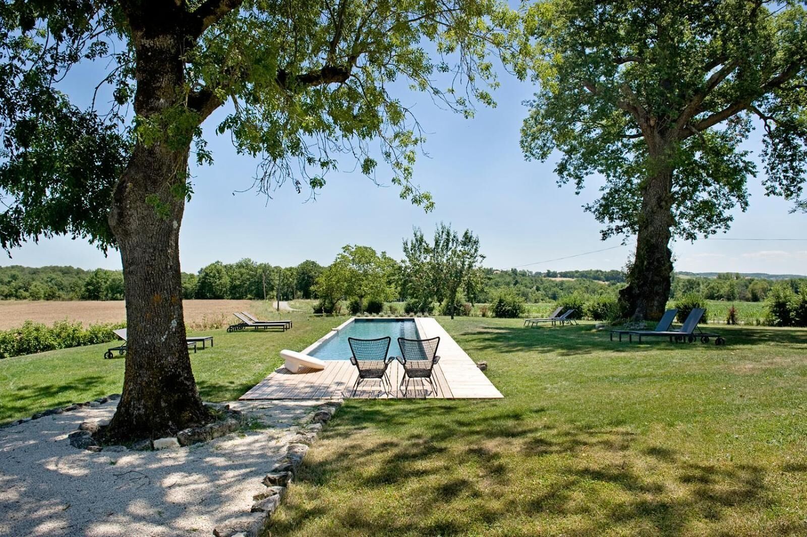 A swimming pool with lounge chairs and a deck area, surrounded by trees and a grassy landscape.
