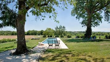 A swimming pool with lounge chairs and a deck area, surrounded by trees and a grassy landscape.