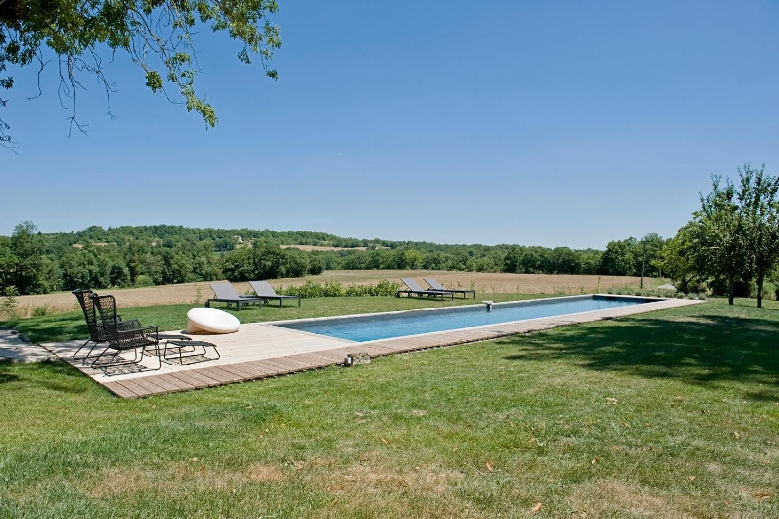 Ein rechteckiger Swimmingpool mit Holzterrasse und Liegestühlen.