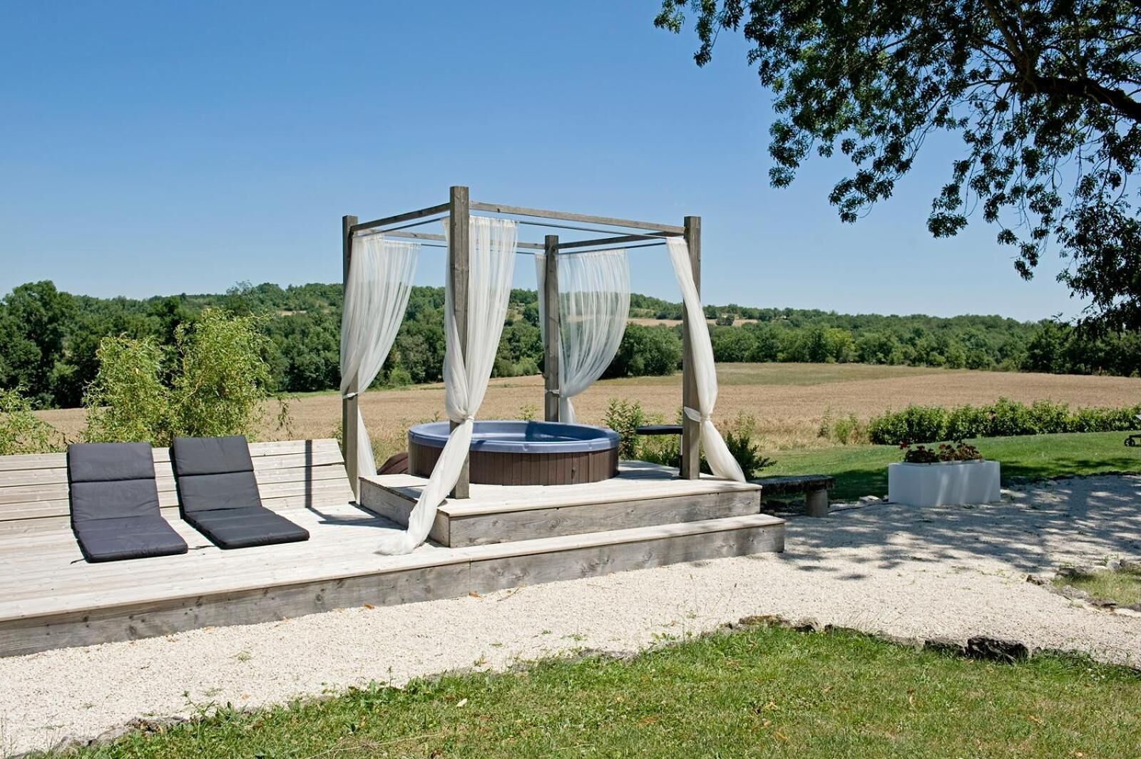 Eine Holzterrasse mit Whirlpool, zwei Liegestühlen und einem Sonnensegel.