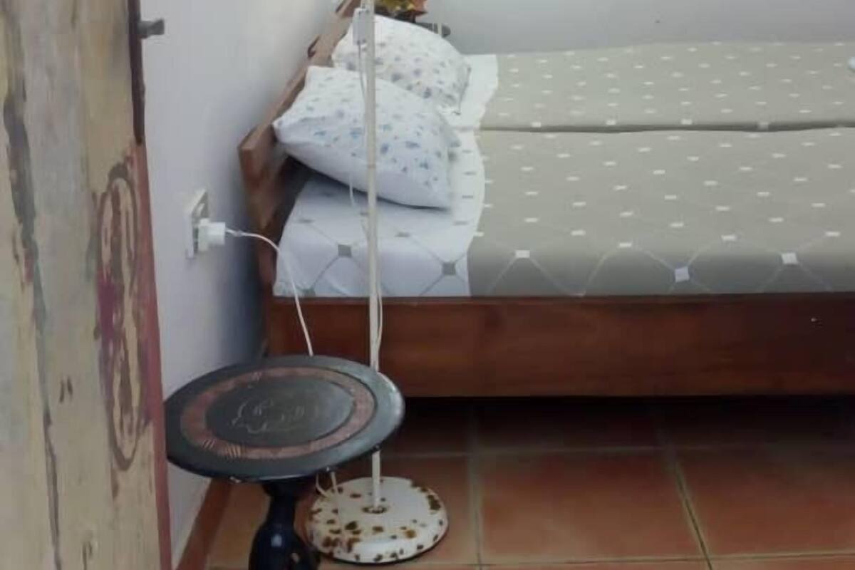 A small, sparsely furnished room with a single bed, a standing lamp, and a small table.