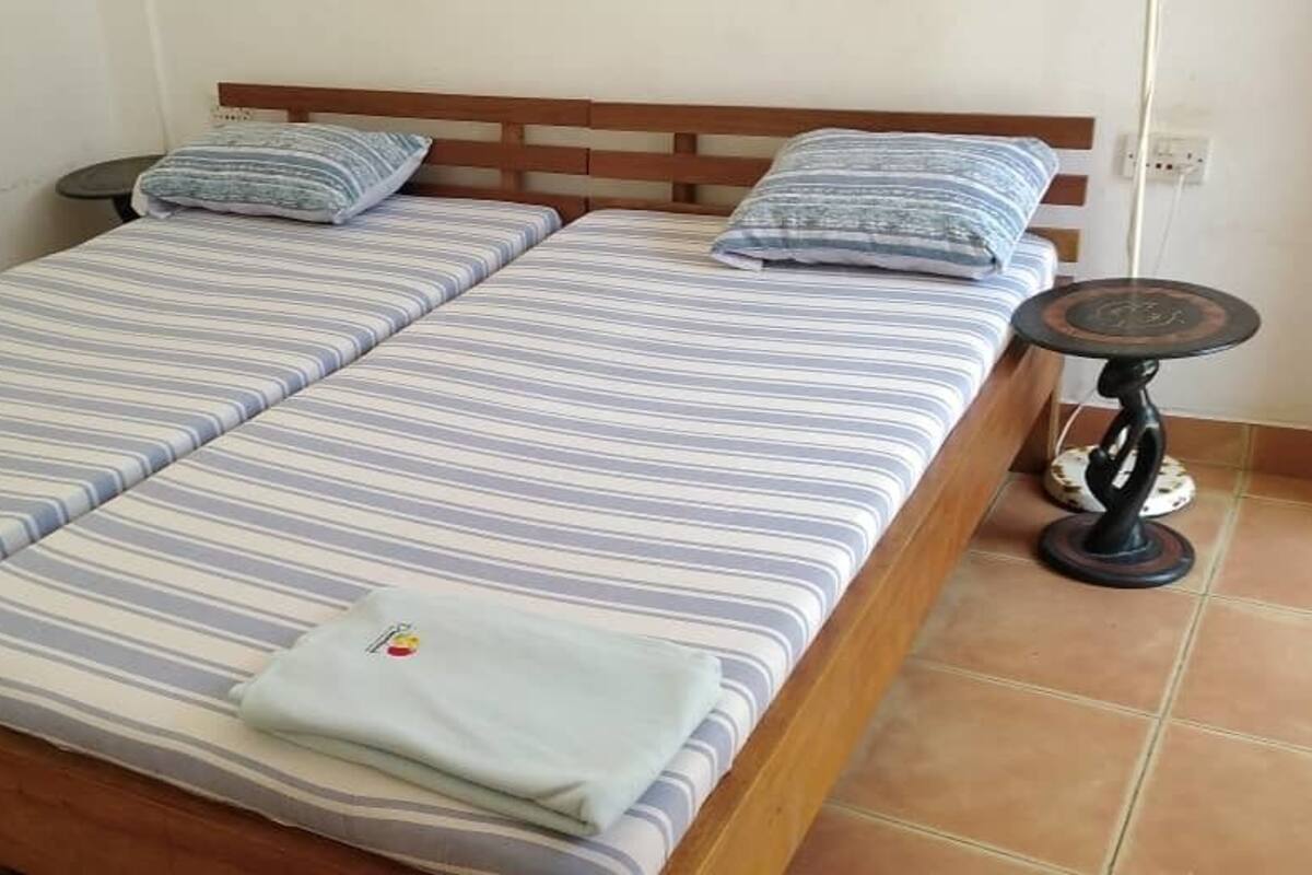 A room with two beds, each with striped bedding and pillows. There is a small round table with a decorative base next to the beds.