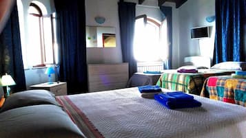 Habitación de hotel con cama, escritorio, silla, televisor y ventana con cortinas.