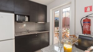 Una cocina moderna con armarios oscuros, un microondas, un lavabo y una cafetera. Hay un vaso de zumo de naranja en la encimera.