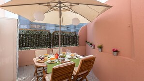 Un comedor con una mesa dispuesta para dos personas, un paraguas grande y plantas en macetas en la pared.