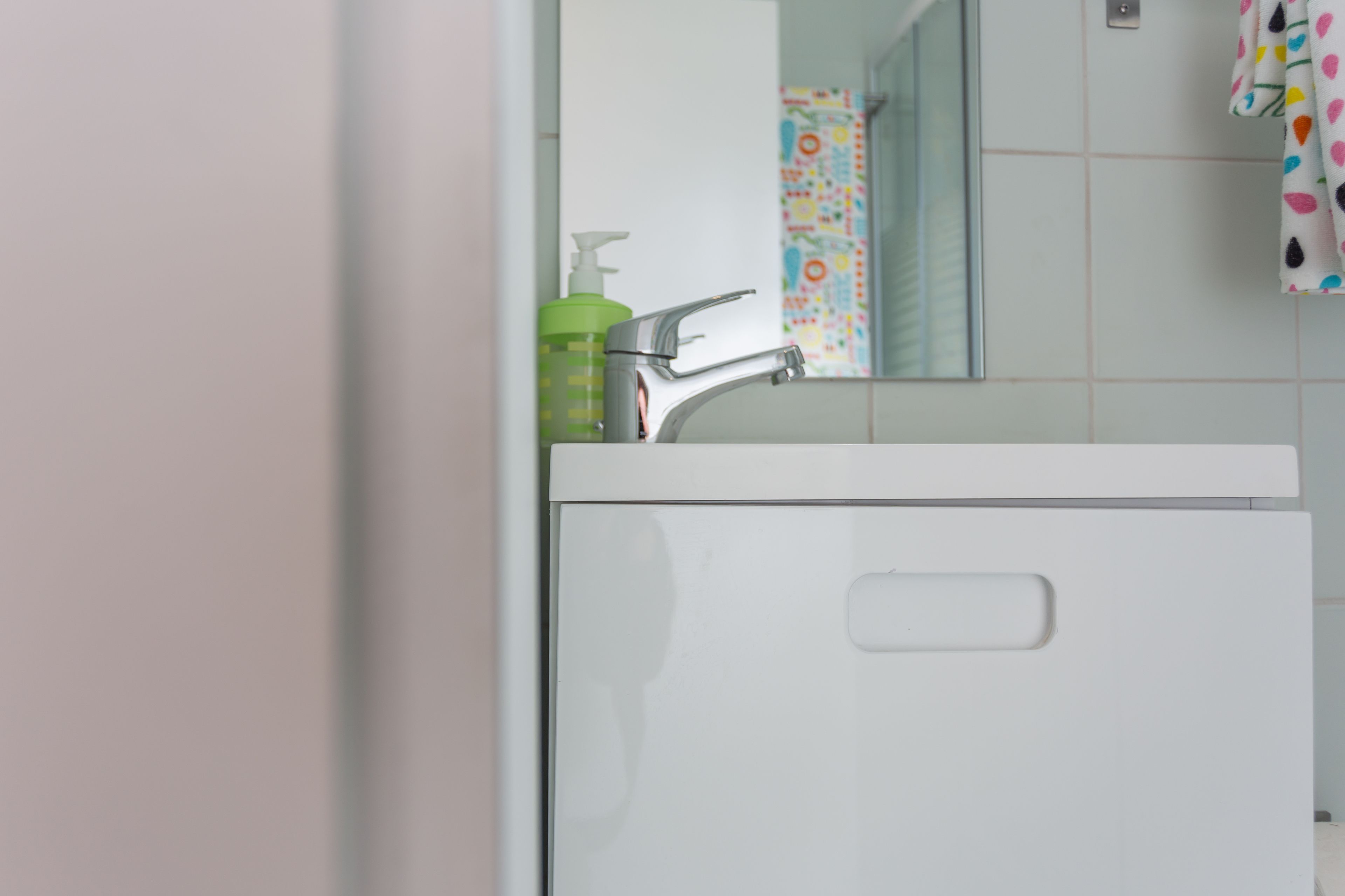 A bathroom with a white sink, a faucet, and a green bottle of hand soap.