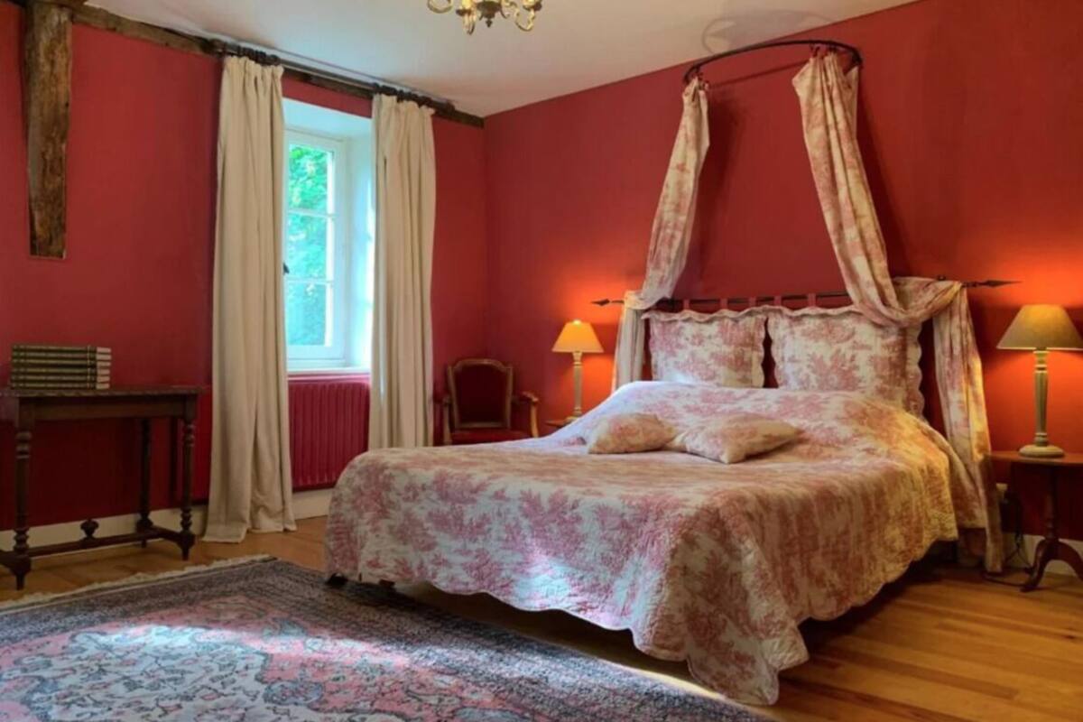 Une chambre à coucher avec un lit à baldaquin, une table de chevet en bois, une chaise et une fenêtre avec des rideaux.