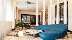 A modern lobby with a blue sofa, a round coffee table, and a dining area with chairs and a table. - Boutique Hotel Health Club&Spa GrandPrix (Astana)