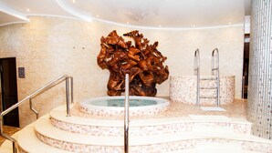 A spa area with a central hot tub, a wooden sculpture, and a set of stairs leading to a shower area. - Boutique Hotel Health Club&Spa GrandPrix (Astana)