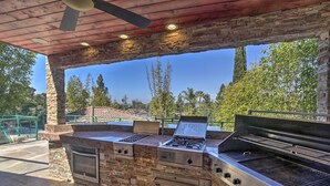 Cocina exterior con diseño de piedra y metal, que incluye una parrilla y un horno empotrado.
