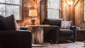 A cozy cabin interior with wooden walls, a round wooden table, two armchairs, and a patterned rug.