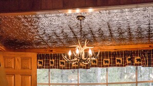 A rustic interior with wooden benches and a table, a chandelier, and a large window with a view of trees.