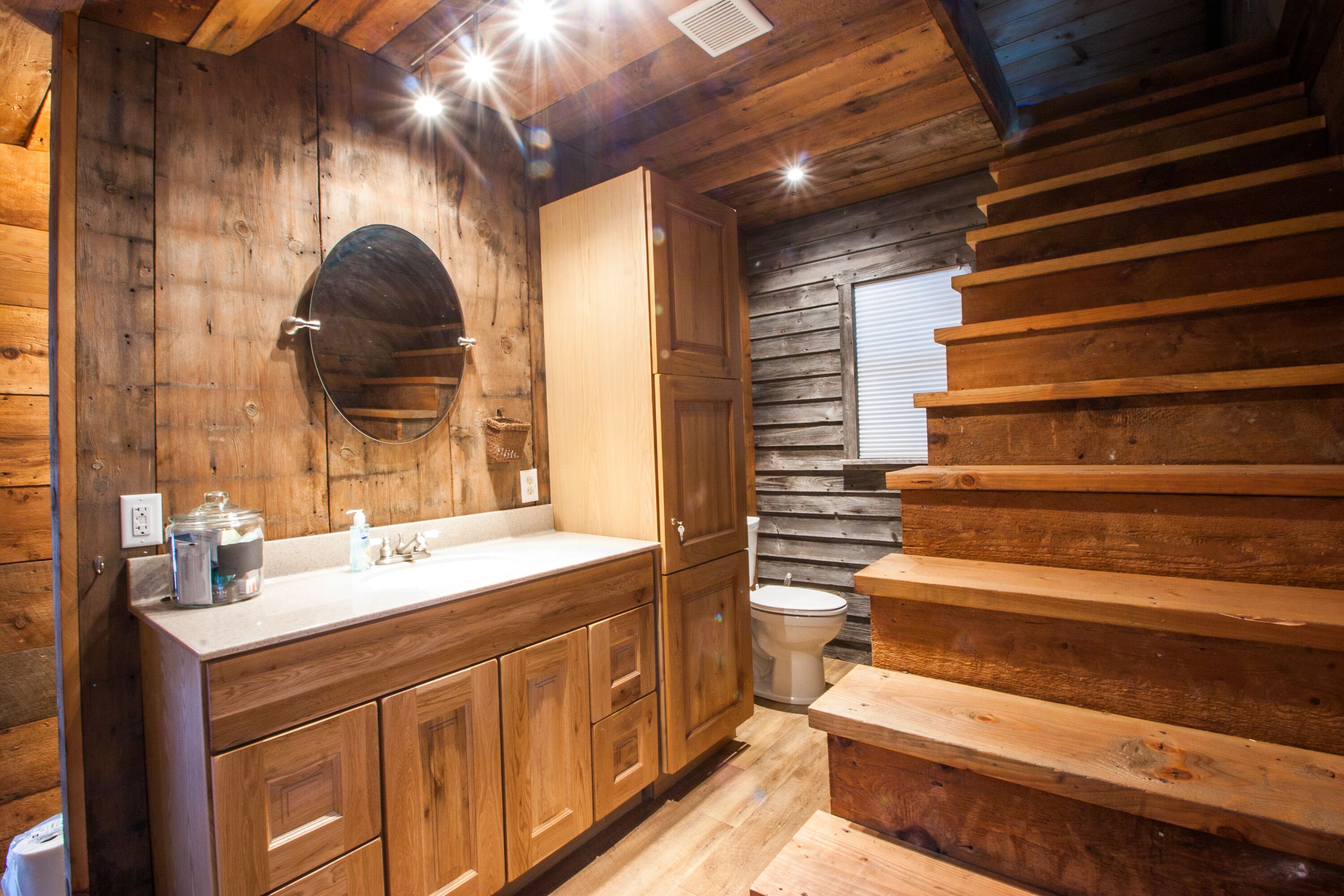 Un baño de estilo cabaña de madera, con tocador de madera, inodoro y una escalera de madera.