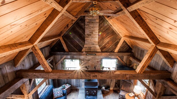 A high-ceilinged wooden interior with a fireplace, seating area, and a ceiling fan.