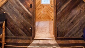 A wooden attic bedroom with a sloped ceiling, a small window, and a wooden door.