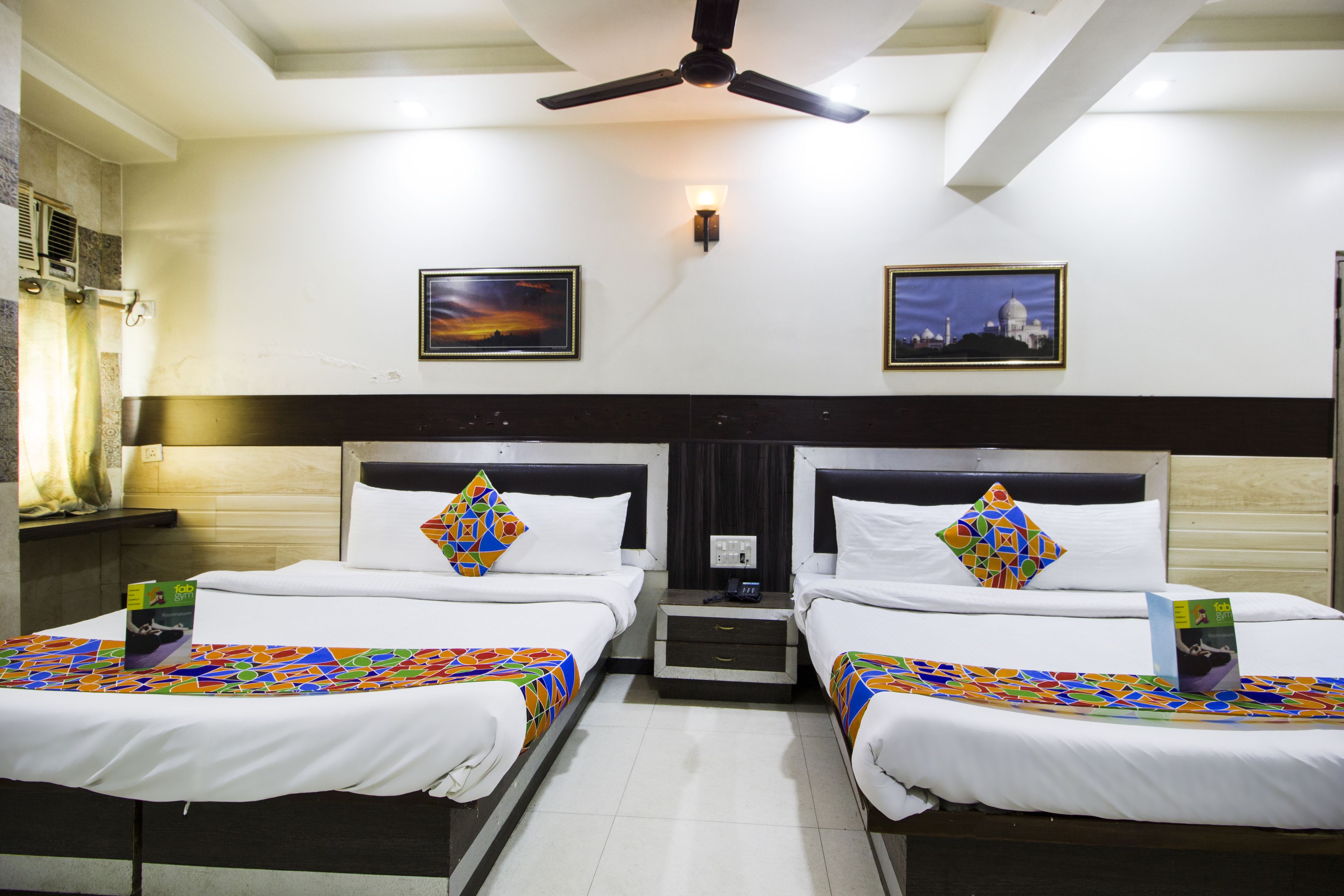 A hotel room with two beds, a ceiling fan, a nightstand, and two framed pictures on the wall.