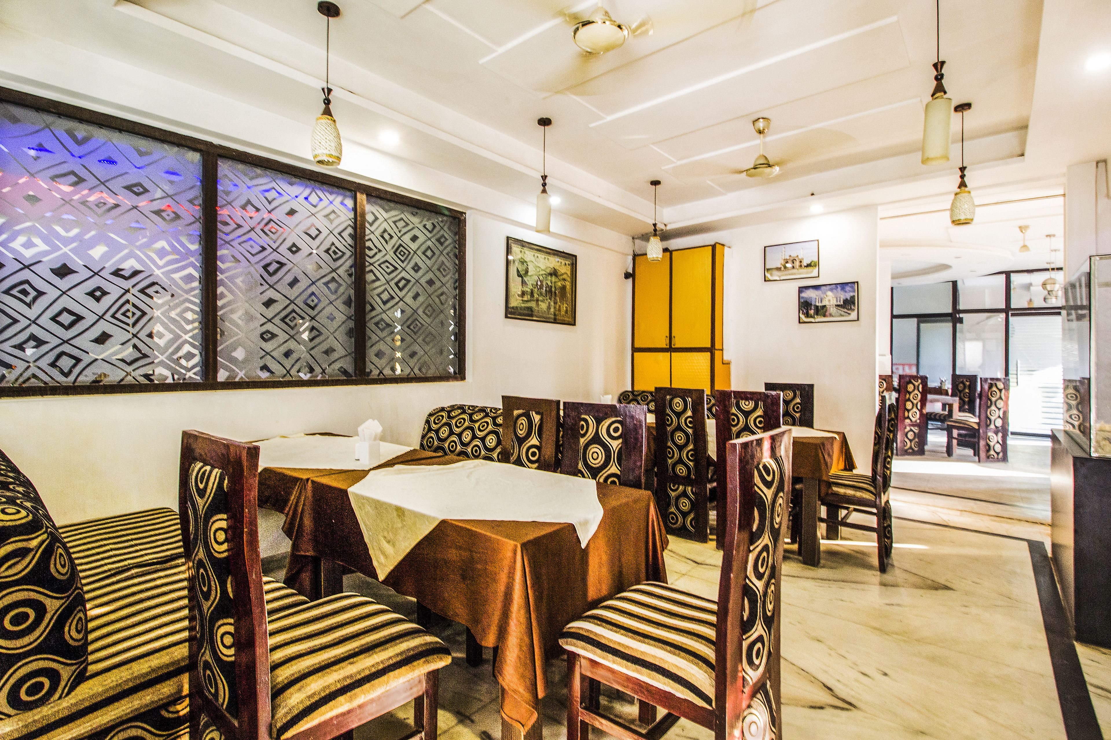 Un restaurante con sillas y mesas estampadas, un muro con diseño y luces colgantes.