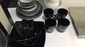 A kitchen counter with black and white plates, bowls, and black mugs.
