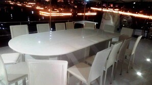 A large oval table with white chairs in a room with a view of a cityscape at night.
