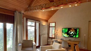 A modern living room with a wooden ceiling, a television, and a dining area. - La Villa dans les Pins (Quend)