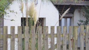 A rustic building with a wooden fence in the foreground, a white exterior wall, and a window with a wooden shutter. - La Villa dans les Pins (Quend)