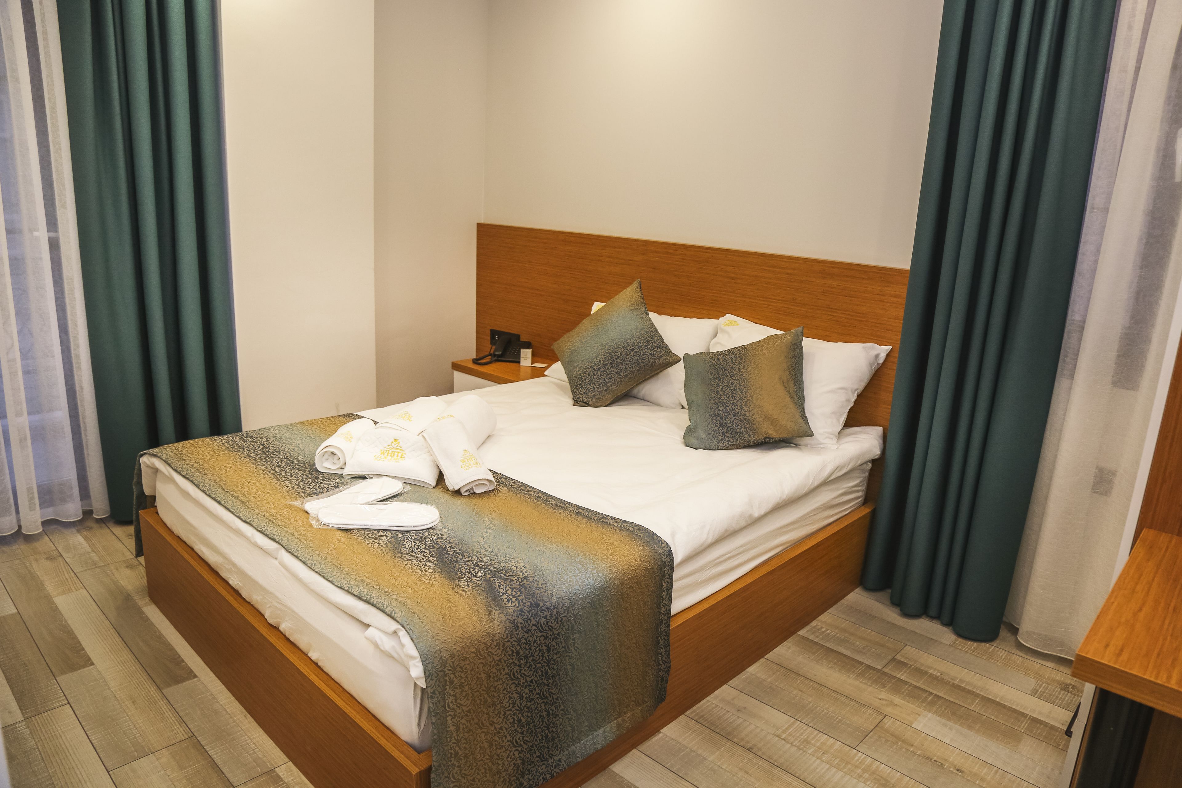 Una cama bien hecha con cabecera de madera, una mesita de noche con un teléfono y un par de toallas.