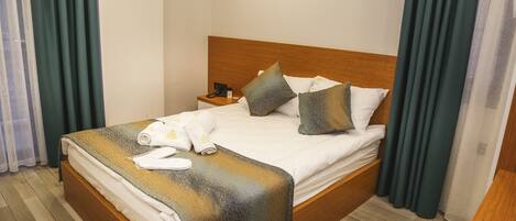 A neatly made bed with a wooden headboard, a bedside table with a phone, and a pair of towels.