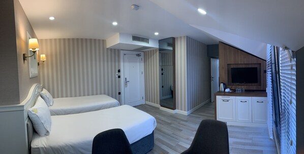 A hotel room with two beds, a TV, a kitchenette, and a bathroom visible through a door.