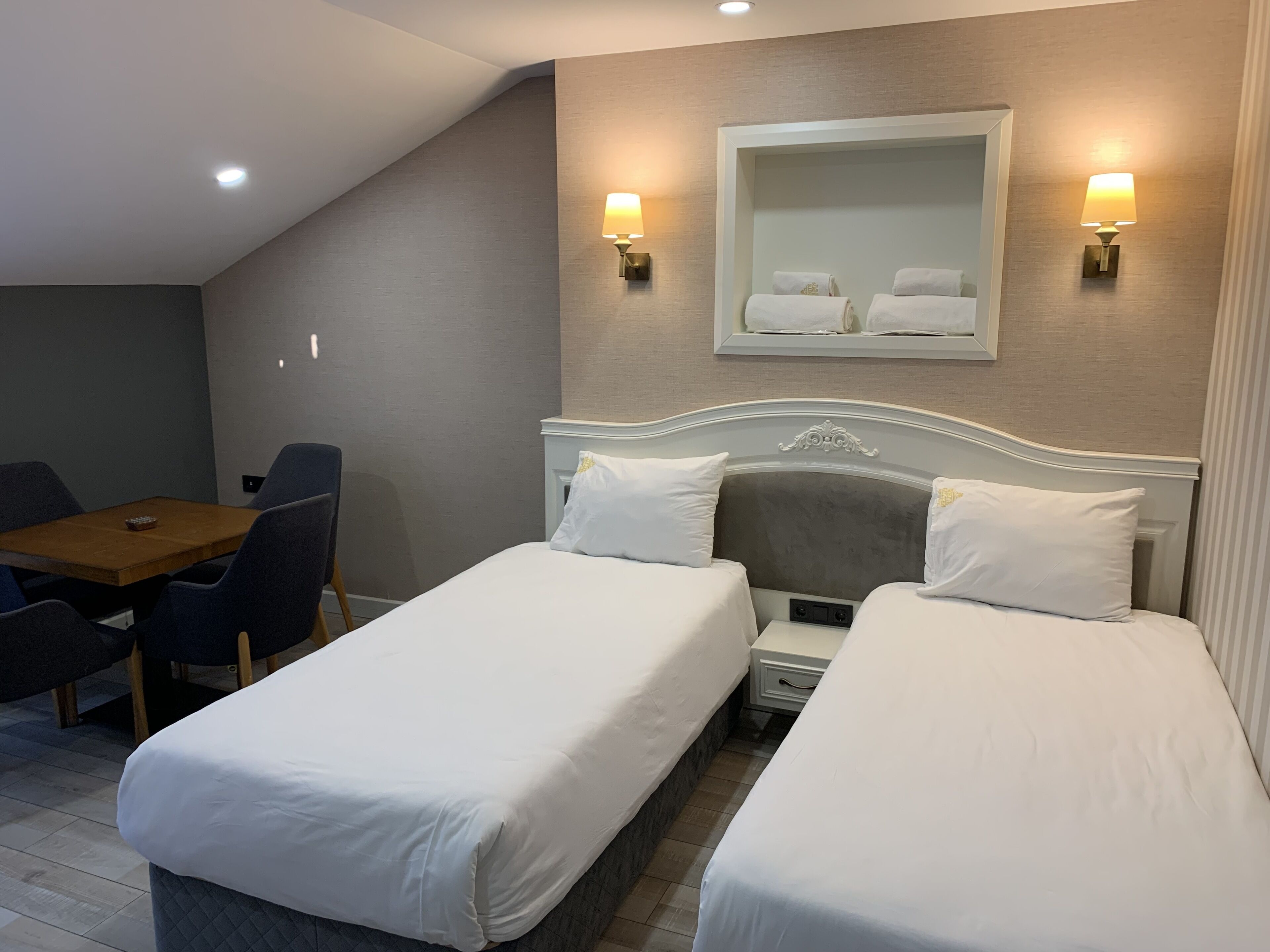 A hotel room with two single beds, a small table, and two chairs.