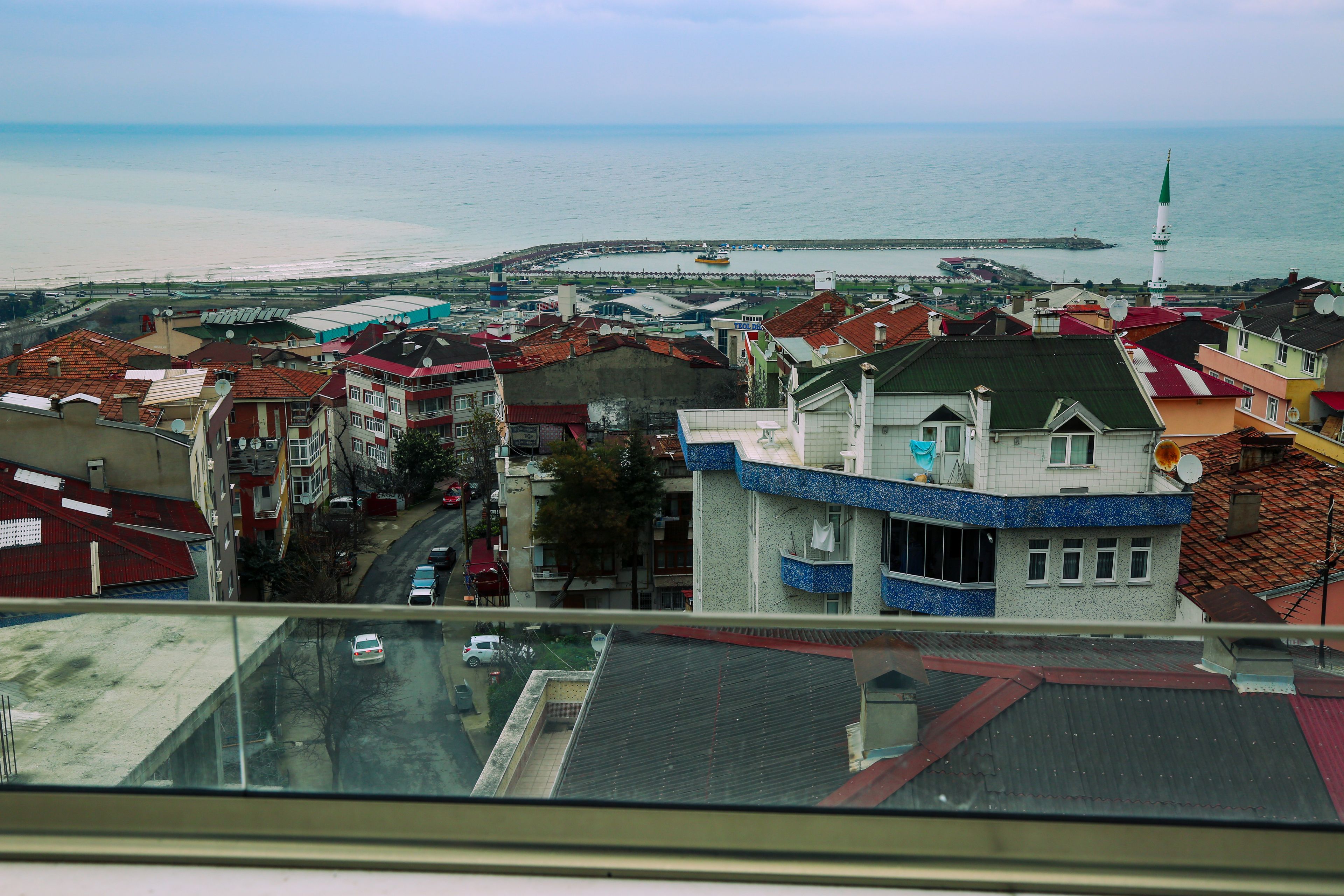 Un paisaje urbano costero con vista al mar, edificios con tejados rojos y azules, y una imponente torre blanca.