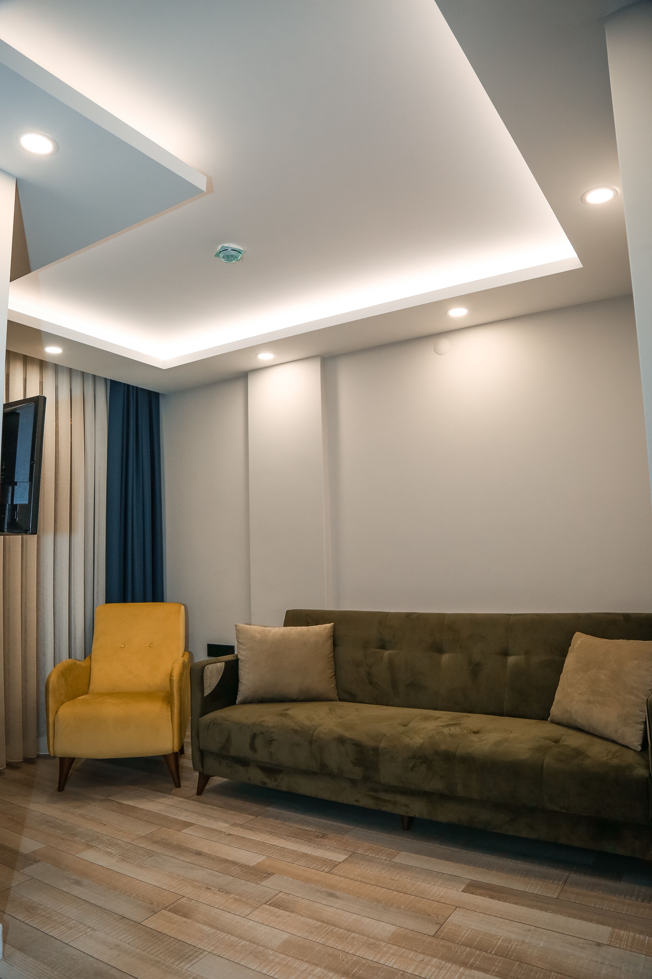 A modern living room with a sofa, a yellow armchair, and a flat-screen TV mounted on the wall.