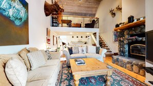 Ein geräumiges Wohnzimmer mit hoher Decke, Kamin, einer Sofagarnitur und einer Treppe, die zu einer oberen Ebene führt.