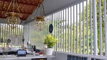 A room with a blue sofa, a wooden ceiling, and a view of greenery through vertical blinds.